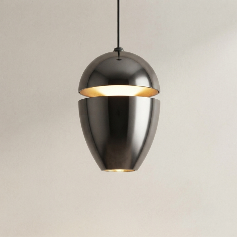 A modern pendant light with a split metallic dome shade in a brushed gunmetal finish, glowing with warm light from within, suspended against a plain light beige wall.