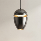 A modern pendant light with a split metallic dome shade in a brushed gunmetal finish, glowing with warm light from within, suspended against a plain light beige wall.