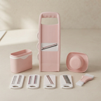 A pink and white multi-functional vegetable chopper and slicer set with multiple interchangeable blades and accessories, arranged neatly on a light beige surface.
