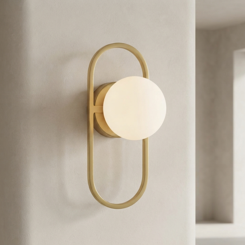 A modern wall sconce with a matte gold metal frame and a glowing frosted white globe shade, mounted on a textured beige wall.