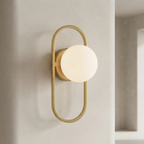 A modern wall sconce with a matte gold metal frame and a glowing frosted white globe shade, mounted on a textured beige wall.