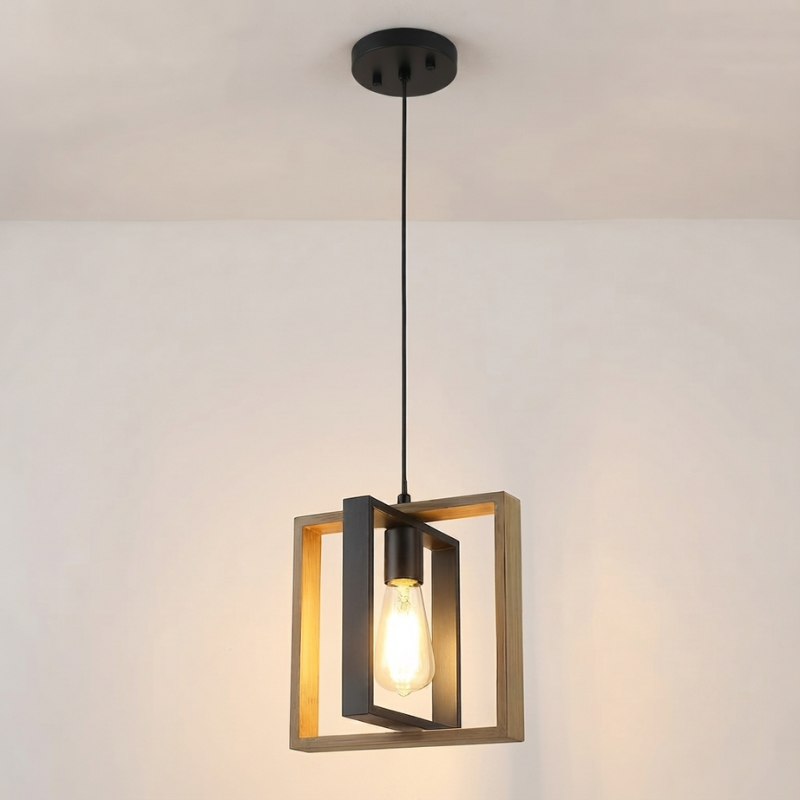 A modern pendant light with a black metal frame and a glowing warm Edison bulb, hanging from a black ceiling canopy against a plain off-white wall.