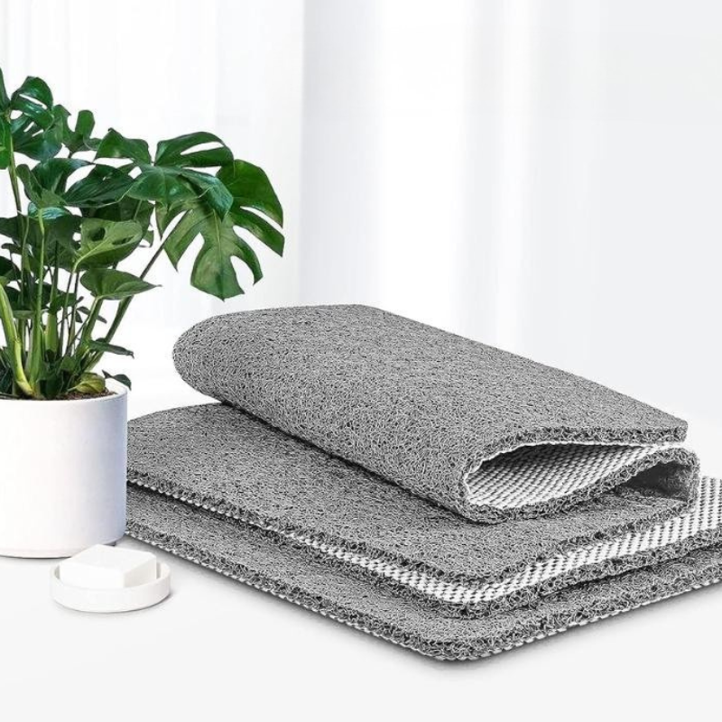 Two gray cleaning cloths stacked on a white surface with a green plant in the background.