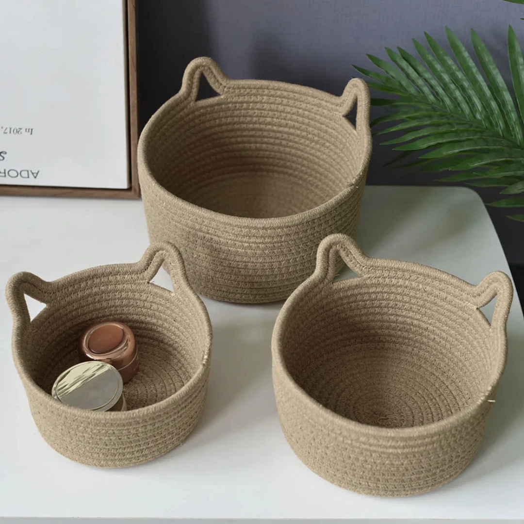 Three woven baskets of different sizes on a white surface with a plant in the background.
