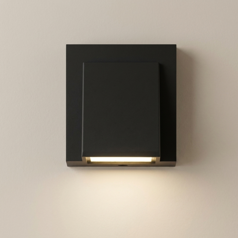 A modern matte black square wall sconce with a built-in horizontal LED light bar, shown mounted on a plain beige wall with the light turned on.