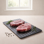 Two raw steaks on a black cutting board with herbs and peppercorns on a light surface.