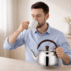 Man drinking from a white mug with a silver teapot in a home setting