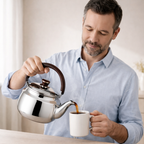 Man pouring tea from a silver teapot into a white mug.
