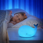 Child sleeping in bed with a whale-shaped night light on the nightstand.