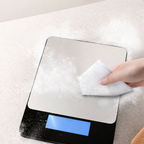 Digital kitchen scale with a hand holding a cloth over it on a textured surface.