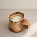 Brown ceramic mug with a hot beverage and whipped cream on a beige surface
