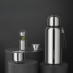Stainless steel tea set with bottle, cups, and strainer on a dark background