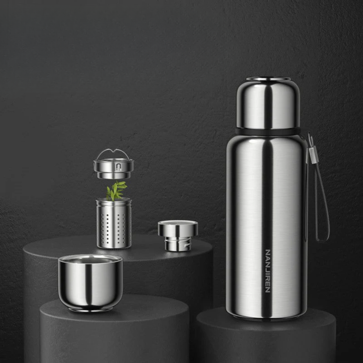 Stainless steel tea set with bottle, cups, and strainer on a dark background