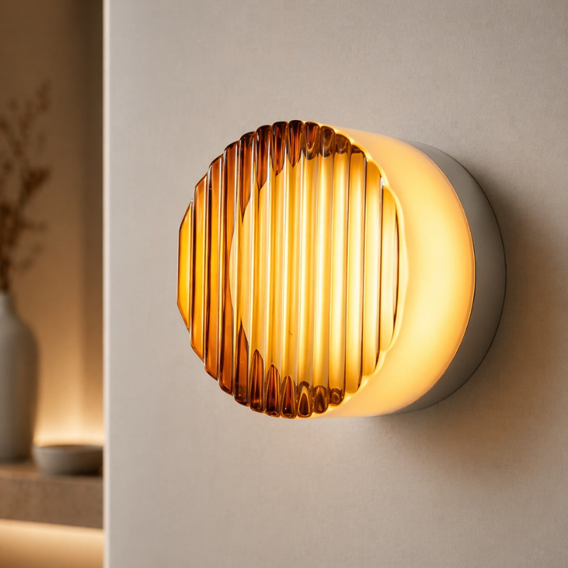 A modern wall-mounted light fixture with a ribbed amber glass shade and a glowing warm white cylindrical body, shown mounted on a beige wall in an interior setting.