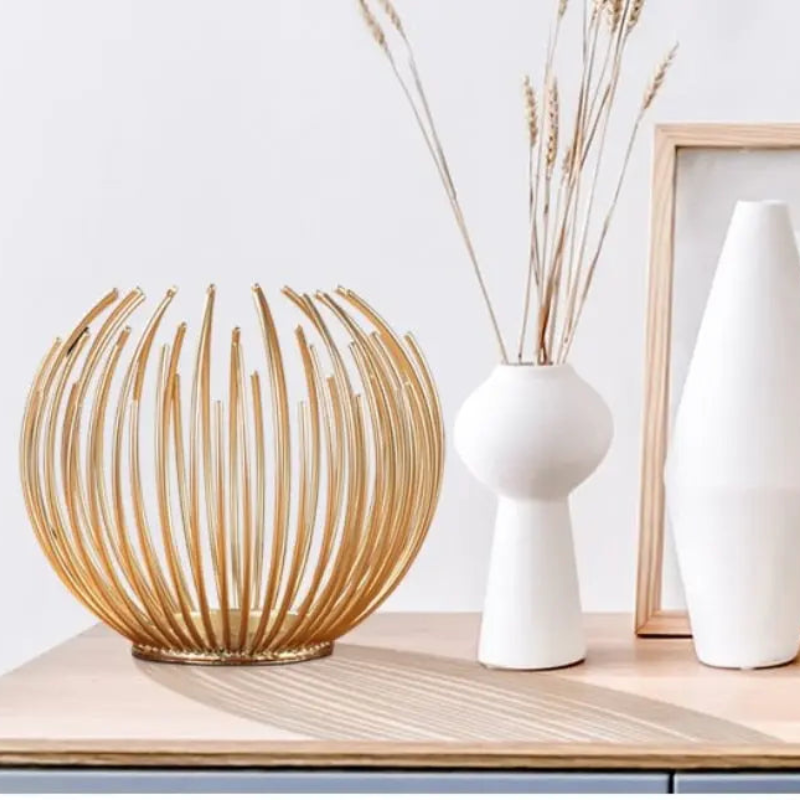 Decorative lamp with gold curved design on a wooden surface, with two white vases and a framed picture in the background.
