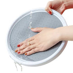 A gray collapsible plastic foot bath with a white rim, shown with water dripping from the top as a hand presses into the bottom. A second hand is holding the rim on a white background.