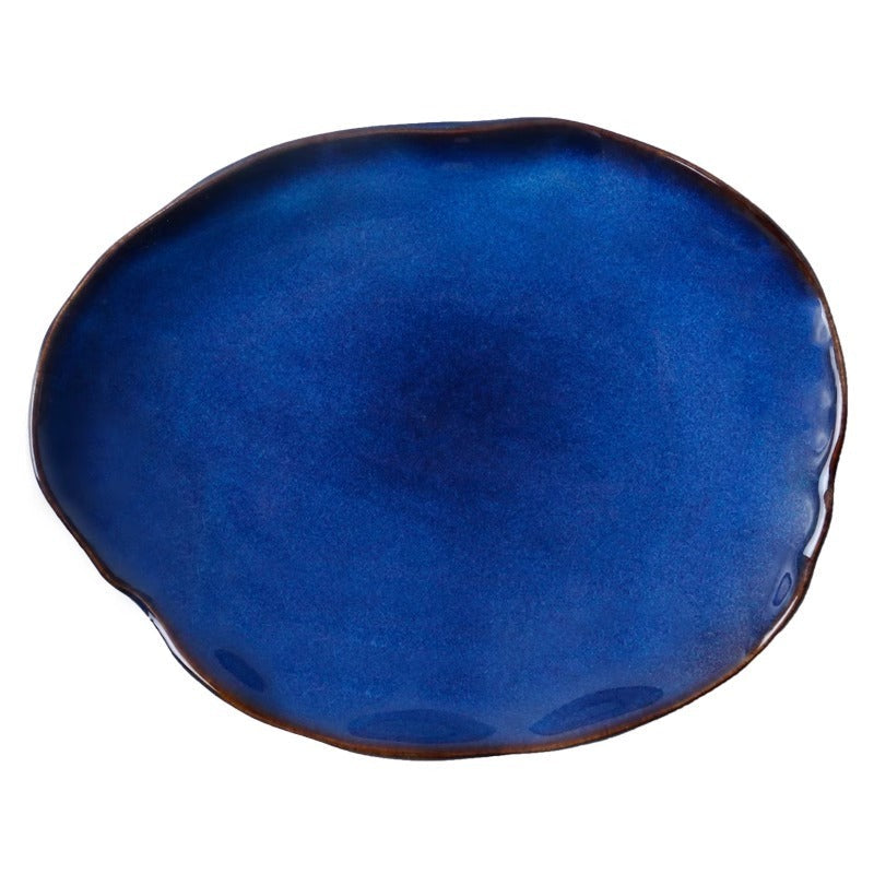 An organic-shaped ceramic plate with a deep cobalt blue glaze and a contrasting dark brown rim, shown on a plain white background.
