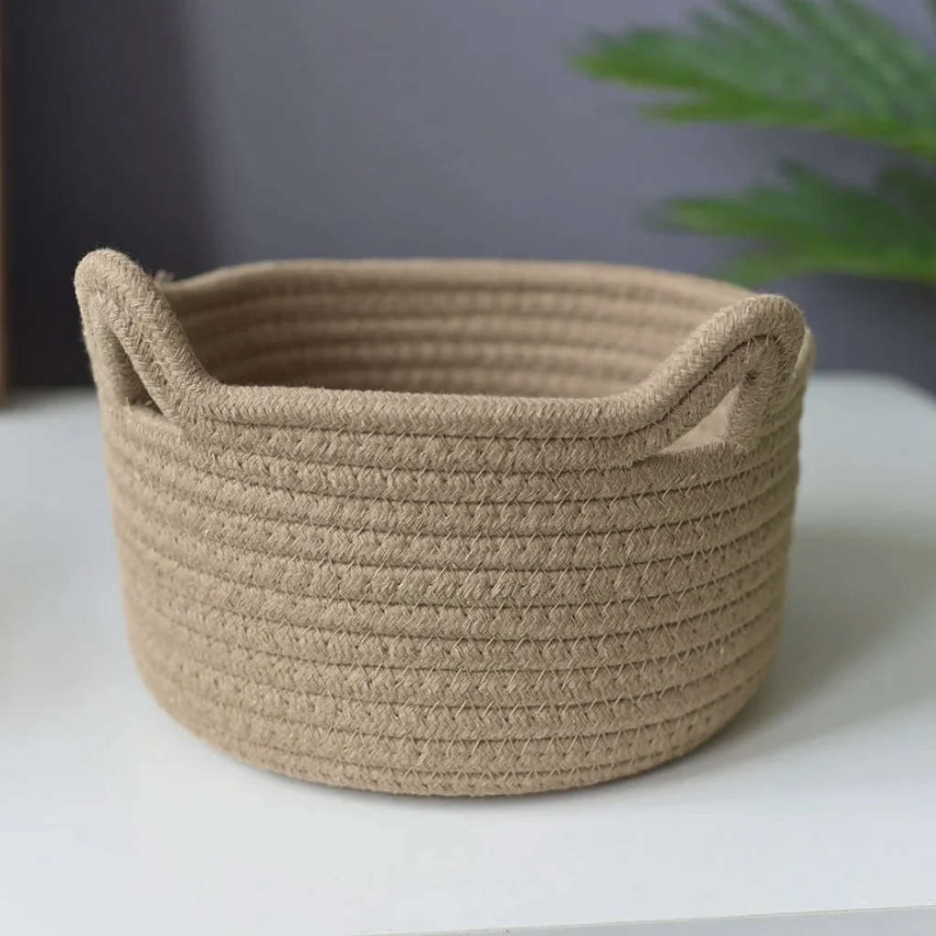 Beige woven basket on a white surface with a blurred green plant in the background