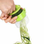 A hand holding a green spiralizer attachment over a clear container, pressing down to extrude long, thin spiral noodles from a cucumber, shown against a white background.
