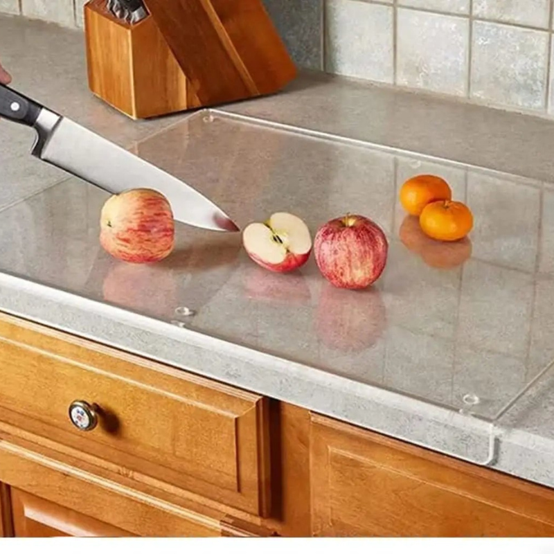 Knife cutting an apple on a metal cutting board with fruits on a wooden countertop.