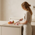 Woman in a kitchen preparing food with fruits on a cutting board.
