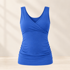 A royal blue sleeveless tank top with a crossover V-neckline and ruched waist details, displayed on a light beige background with soft shadow overlays.