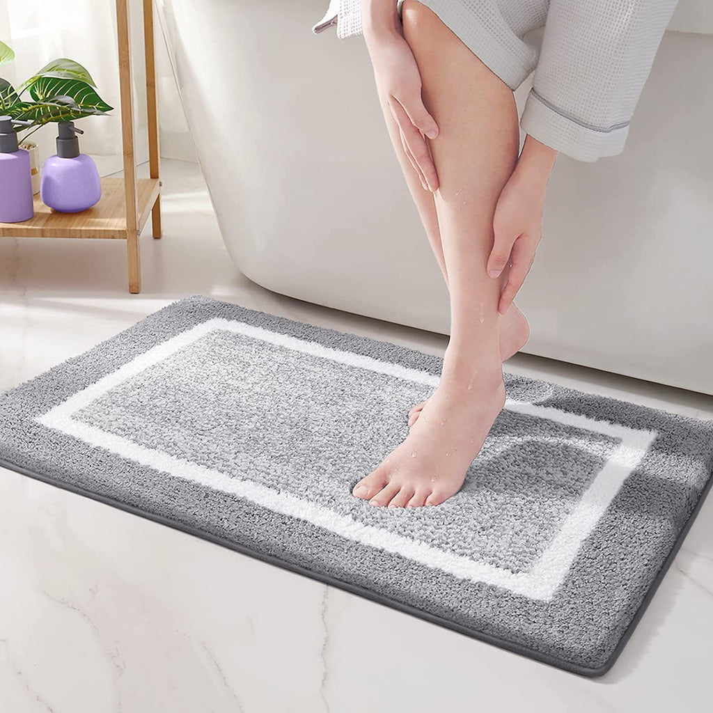 Person stepping onto a gray bath mat with a white border in a bathroom setting.