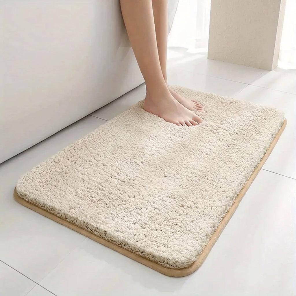 Beige bath mat on a white floor with a person's foot stepping onto it.