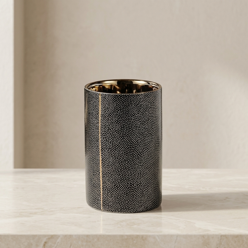 A cylindrical black shagreen candle tin with a gold interior, standing on a light marble surface against a neutral beige background.