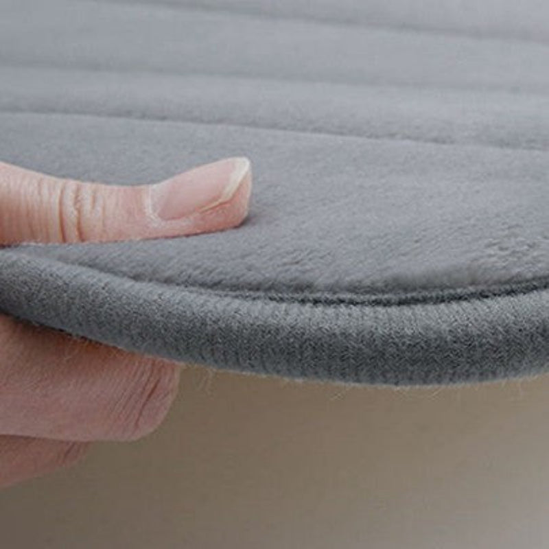 A close-up of a gray textured cushion or pad being held down by a person's fingers to show its thickness and soft texture.