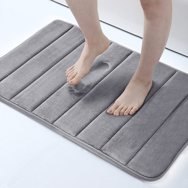 Person stepping onto a gray bath mat on a light background