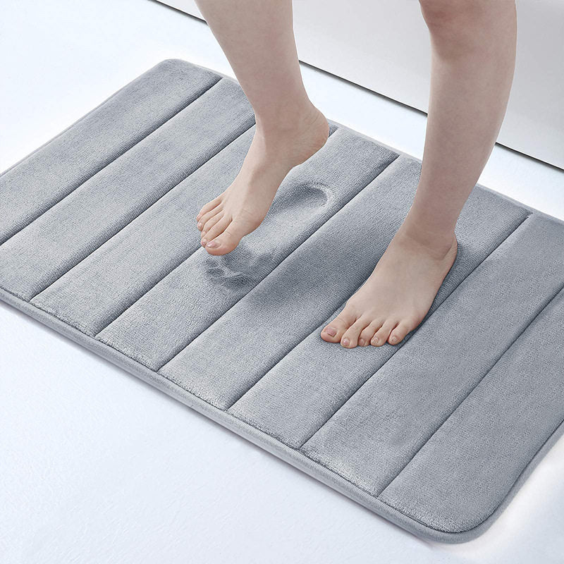 Person stepping onto a gray bath mat on a white floor