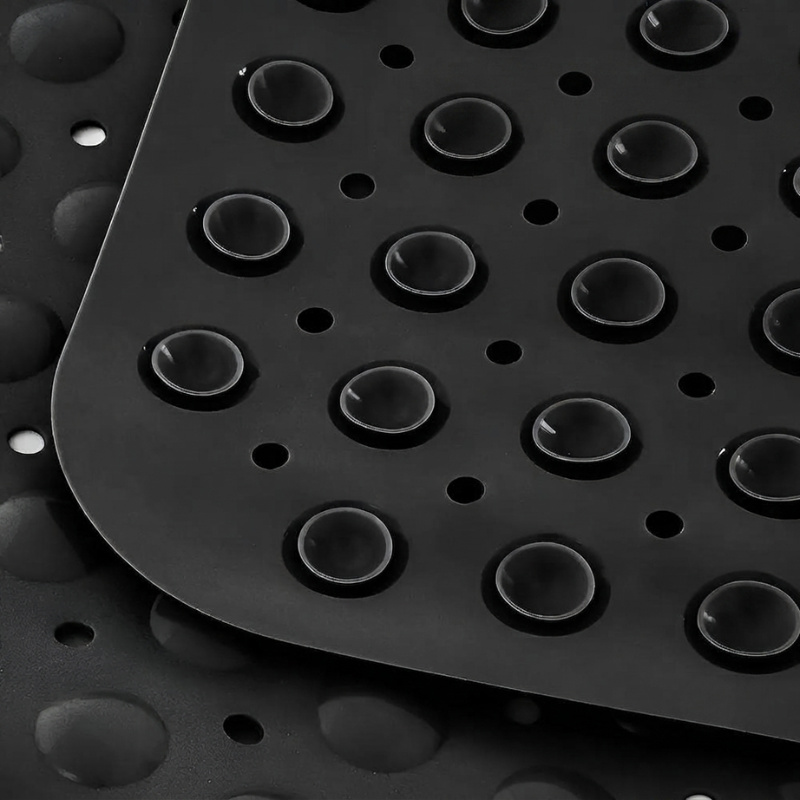 Close-up of a black textured rubber mat with raised circular bumps and drainage holes, layered over a similar mat in the background.