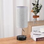 Table lamp with a gray shade on a wooden surface next to books and a plant.
