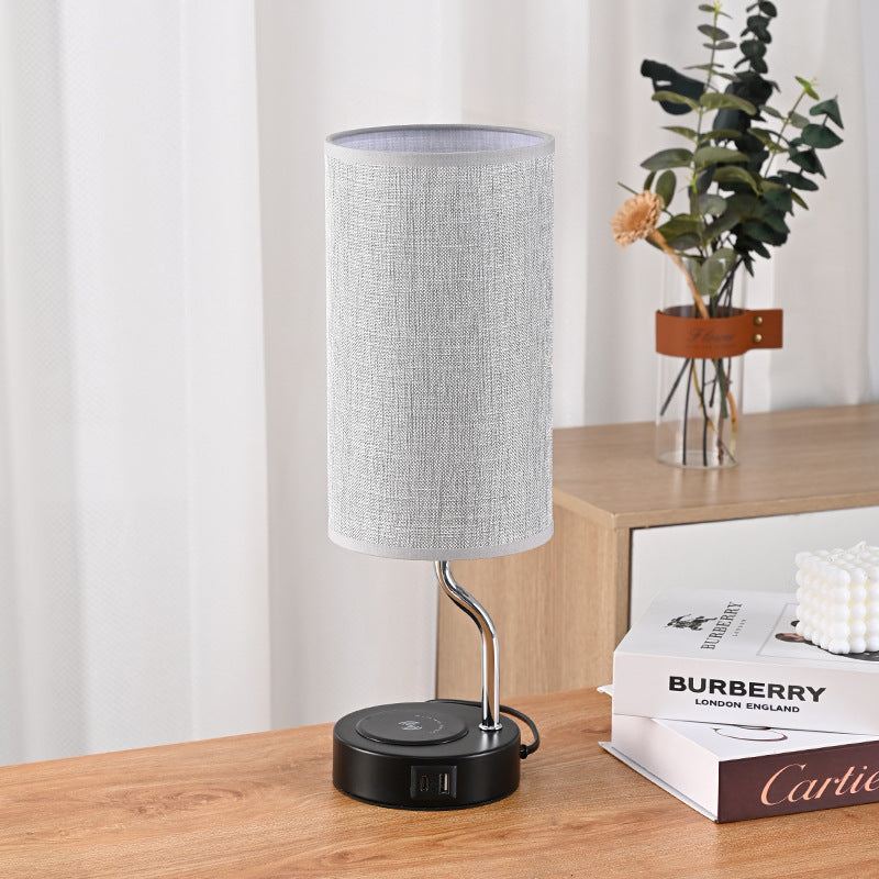 Table lamp with a gray shade on a wooden surface next to books and a plant.
