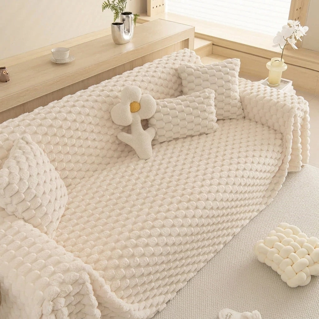 A cream-colored textured knit sofa cover with matching throw pillows and a flower-shaped cushion, styled on a sofa in a bright, modern room.