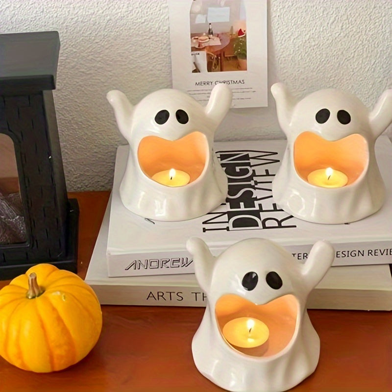 Three white ghost-shaped candle holders with black eyes and open mouths, each holding a lit tea light candle, arranged on stacked books with a small orange pumpkin in the foreground.