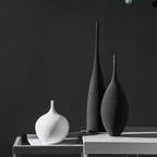 Three textured ceramic vases in white and dark charcoal gray, styled on a minimalist white table against a dark gray background.