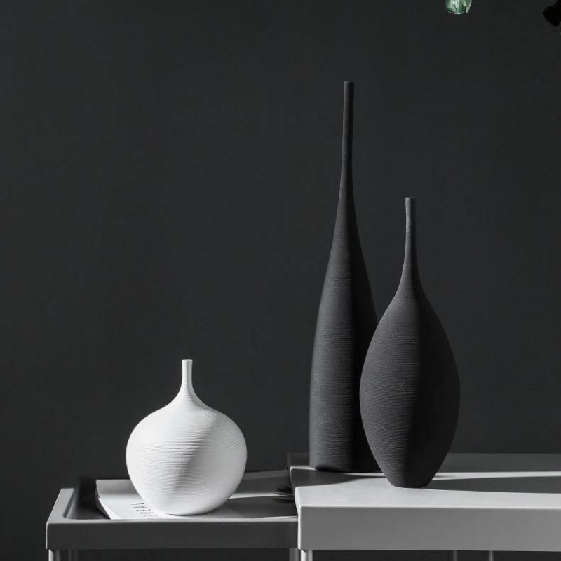 Three textured ceramic vases in white and dark charcoal gray, styled on a minimalist white table against a dark gray background.