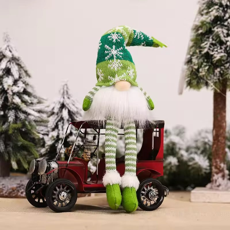 Gnome in a green hat and striped pants sitting on a small red car with a snowy background