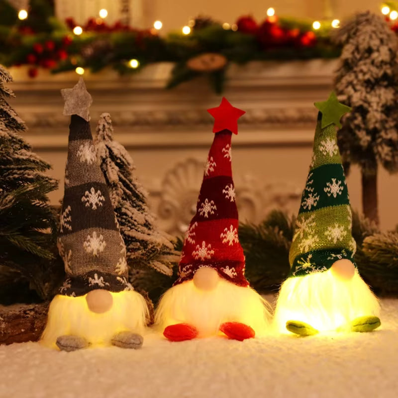 Three Christmas gnome floor lights arranged in a row on a snowy surface, glowing warmly. The gnomes have tall knit hats in gray, red, and green with white snowflakes, white beards, and small gray, red, and green feet.