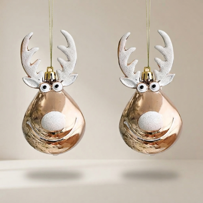 Two Christmas tree ornaments shaped like reindeer heads, hanging against a plain beige background. The ornaments have shiny metallic rose-gold bodies, textured white antlers, and white snouts with black eyes.