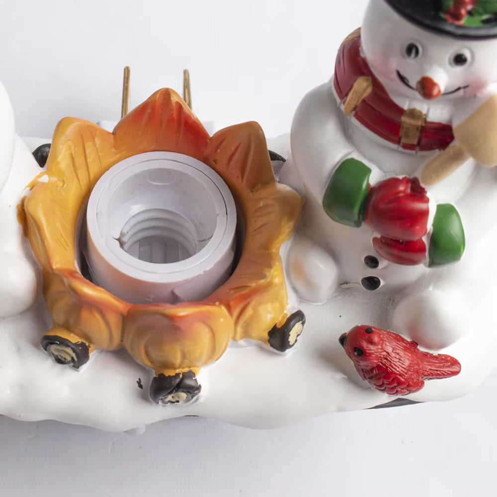 A close-up of a holiday-themed decorative light fixture or ornament featuring a snowman, a small red bird, and a flame-shaped socket on a white snowy base.