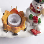 A close-up of a holiday-themed decorative light fixture or ornament featuring a snowman, a small red bird, and a flame-shaped socket on a white snowy base.