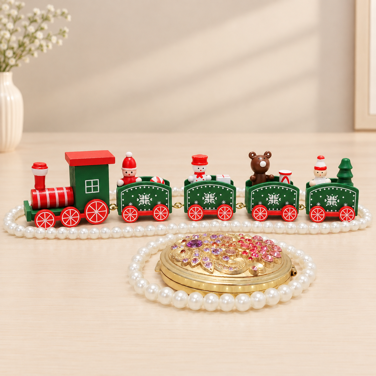 A decorative toy train set displayed on a light wood surface with a pearl-like circular frame in front. The train has a red engine car and green passenger cars with red wheels, white snowflake details, small holiday figures, and a brown bear decoration.