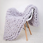 Cozy chunky knit blanket draped over a white chair on a light gray background