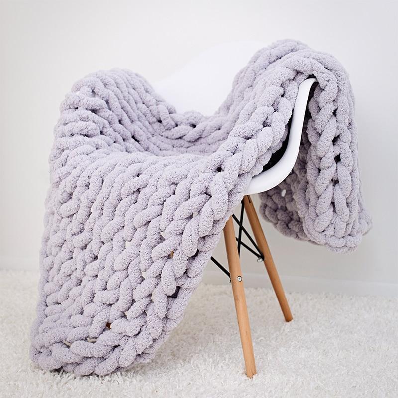 Cozy chunky knit blanket draped over a white chair on a light gray background