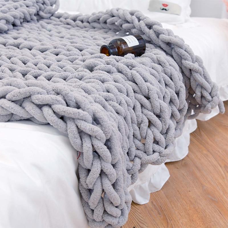 Gray chunky knit blanket draped over a bed with a small bottle on top.