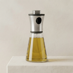 Glass oil dispenser with metal top on a neutral background