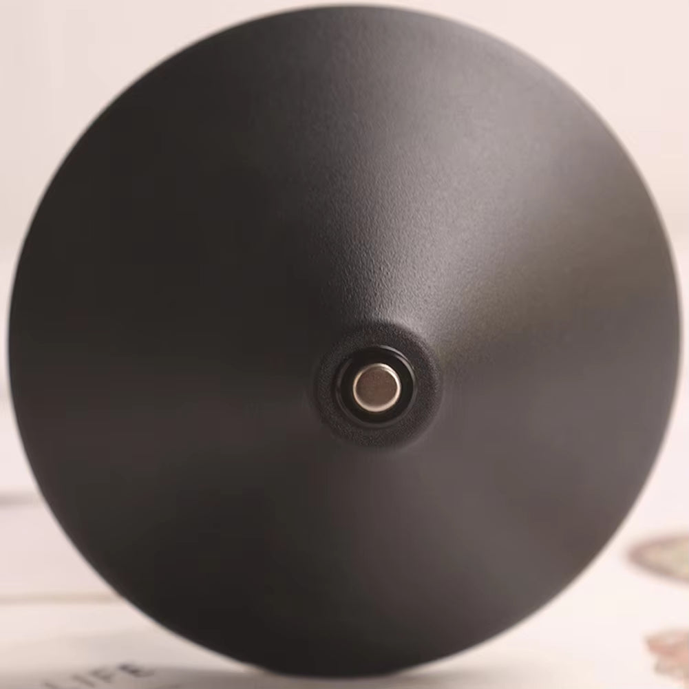 A close-up of a matte black dome-shaped object, likely a lamp shade or decorative dome, with a small metallic circular detail at the center, set against a light beige background.